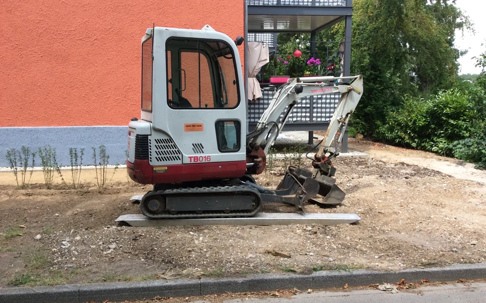 Mini-escavadora de rastos com cabina e balde numa obra.